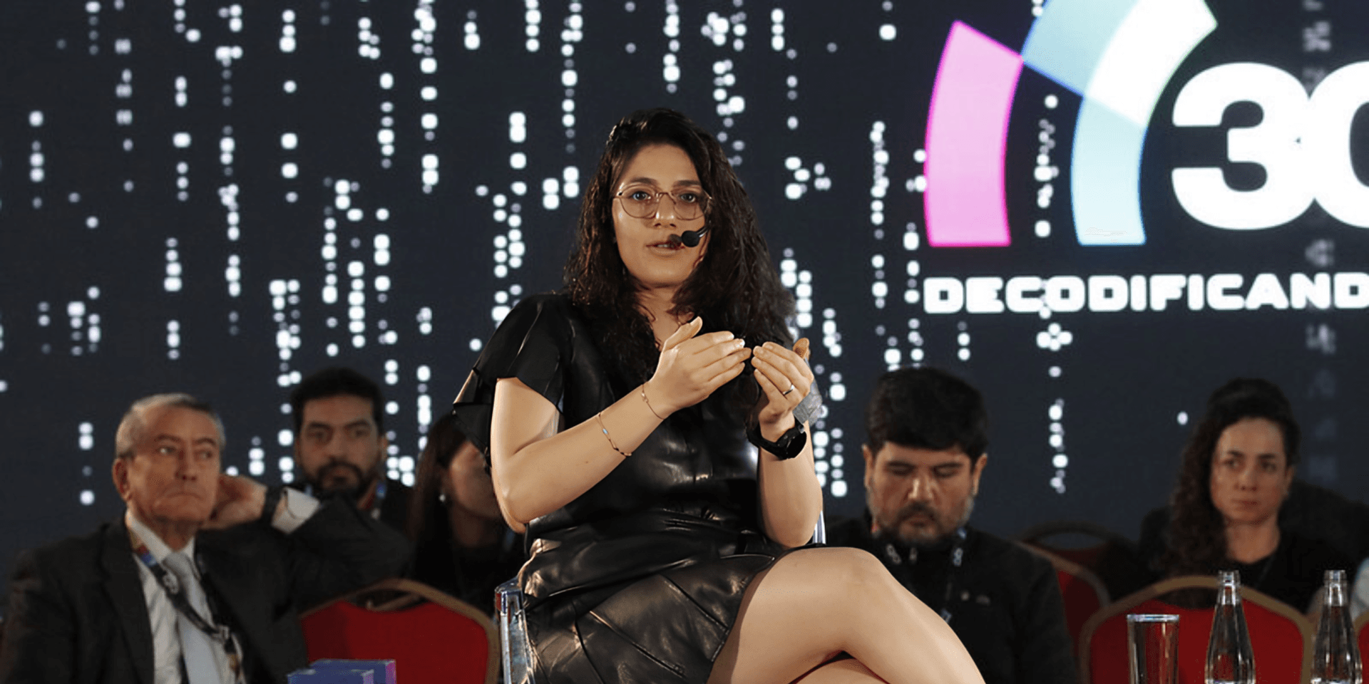 A speaker presents on stage at a conference with an audience in the background