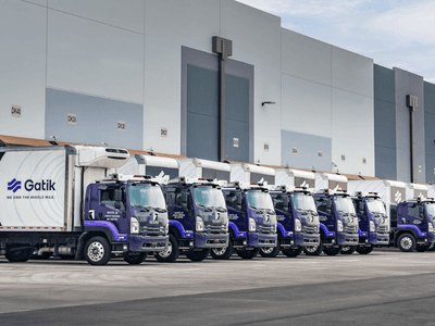 A fleet of autonomous delivery trucks lined up alongside a warehouse loading dock