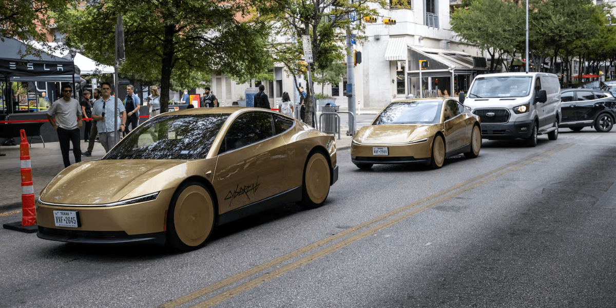 Two gold-colored electric cars on a city street with pedestrians and vehicles nearby