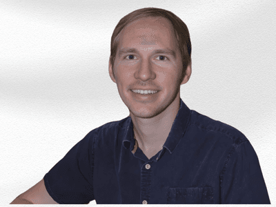 Smiling man with short hair wearing a dark blue shirt against a white background