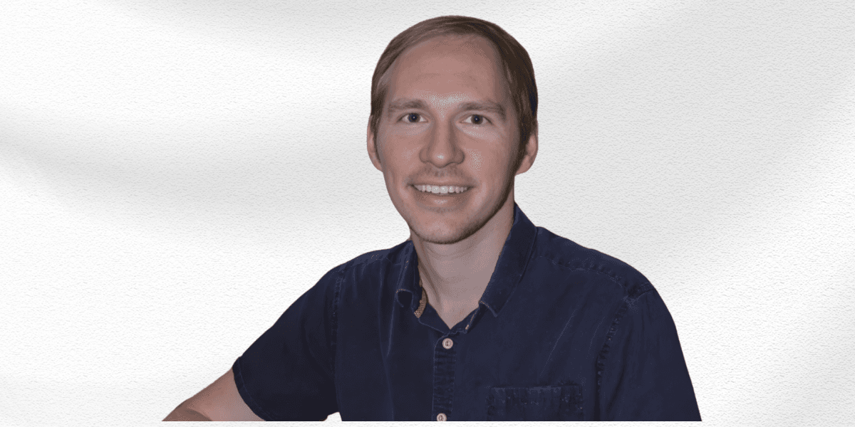 Smiling man with short hair wearing a dark blue shirt against a white background