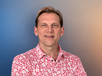A smiling man in a floral shirt poses against a gradient background