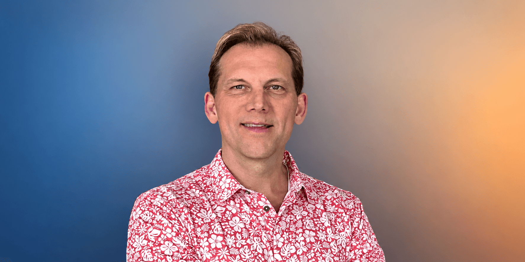 A smiling man in a floral shirt poses against a gradient background