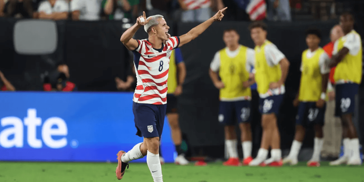 Soccer player celebrating a goal, wearing a striped jersey, with teammates in background